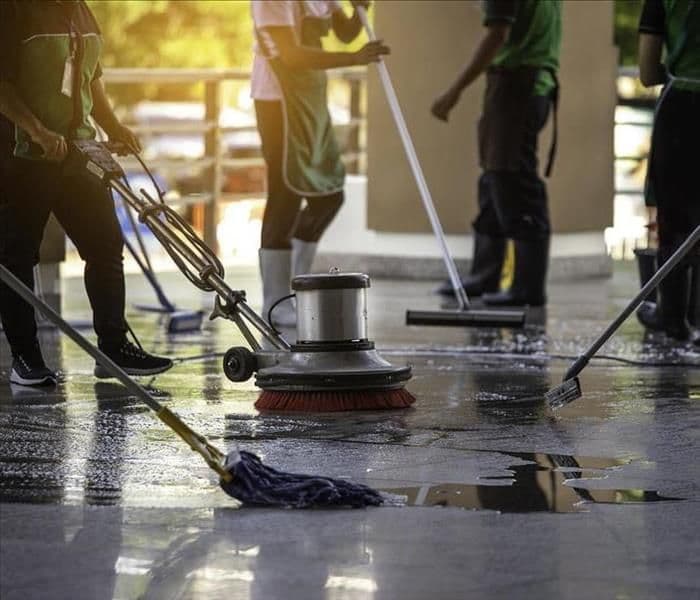 Cleaning team covering a large institutional floor with a buffer and mops
