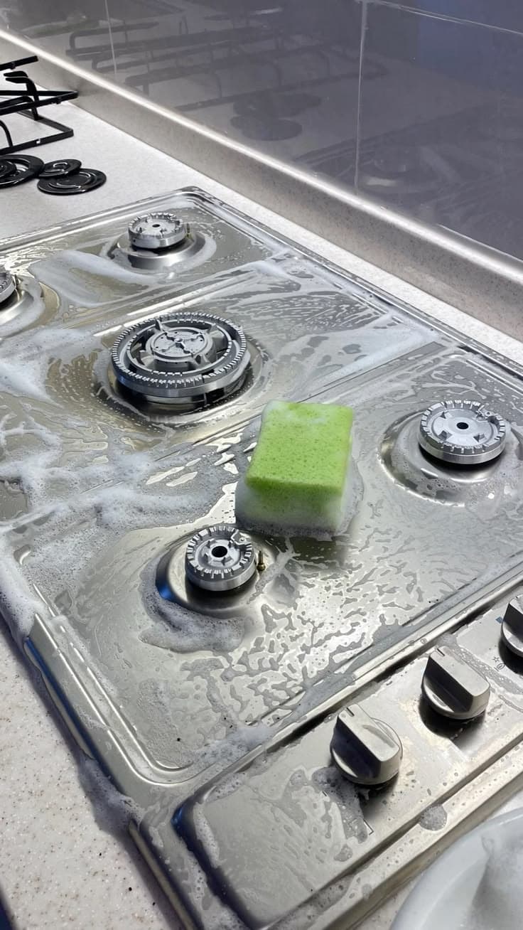 Gas cooker top being degreased with a soapy sponge