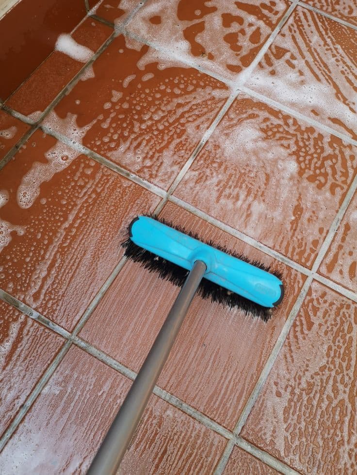 Deck brush scrubbing suds across terracotta floor tiles